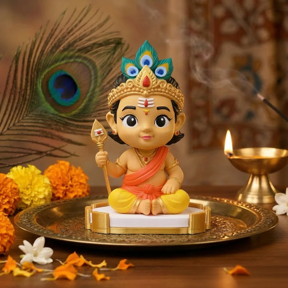 Small statue of a Bala Murugan on a decorative tray with flowers and a peacock feather.